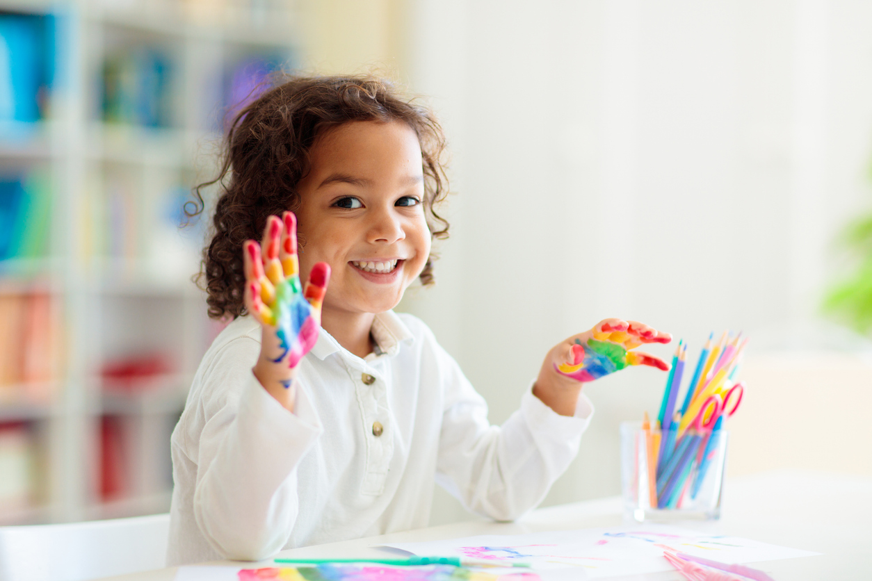 Child drawing rainbow. Paint on hands. Remote learning and online school art homework from home. Arts and crafts for kids. Little boy drawing bright picture. Creative kid playing and studying.